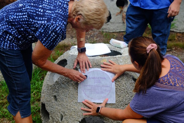 family making chalk rubbing of bronze placard on reef ball