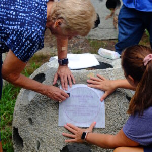 family making chalk rubbing of bronze placard on reef ball