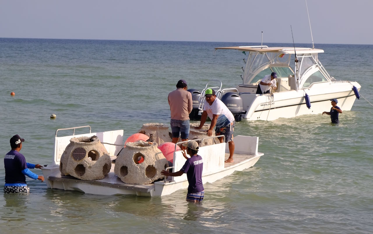 crew towing reef balls out to sea using a raft and boat